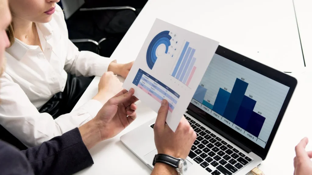 Two people sit at a table reviewing charts and graphs